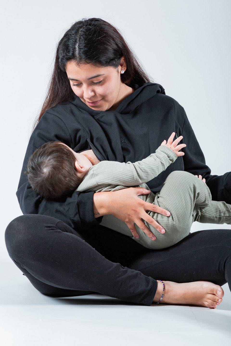 Polerón de lactancia negro con capucha y cierres laterales, modelo oversize, usado por mujer mientras amamanta a su bebé.