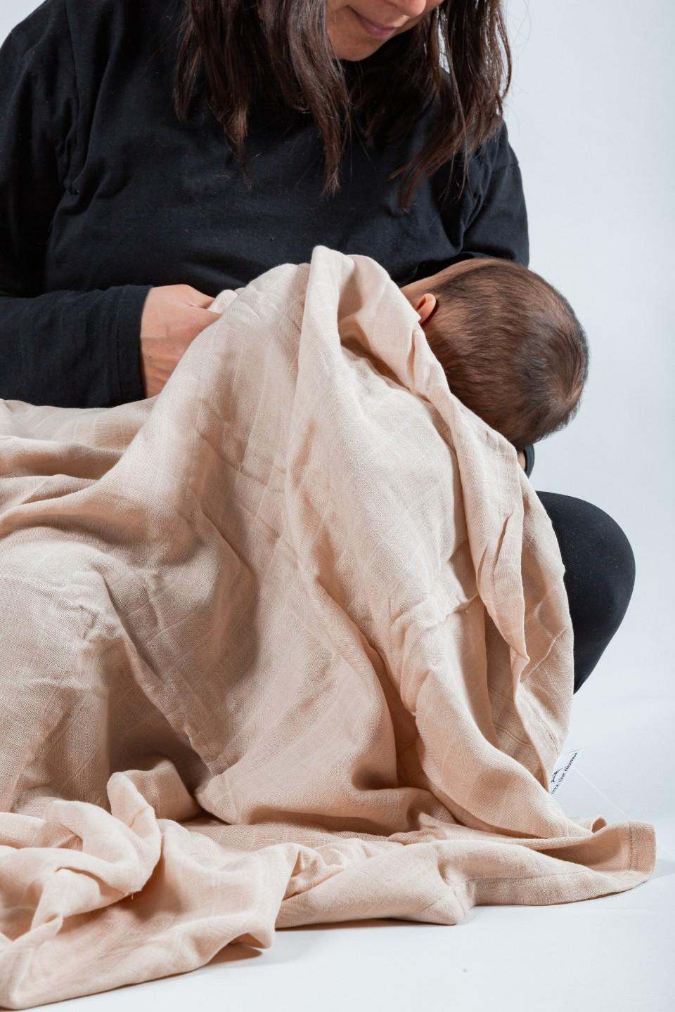 Mujer sosteniendo a un bebé envuelto en una manta de muselina beige, destacando su suavidad y confort.